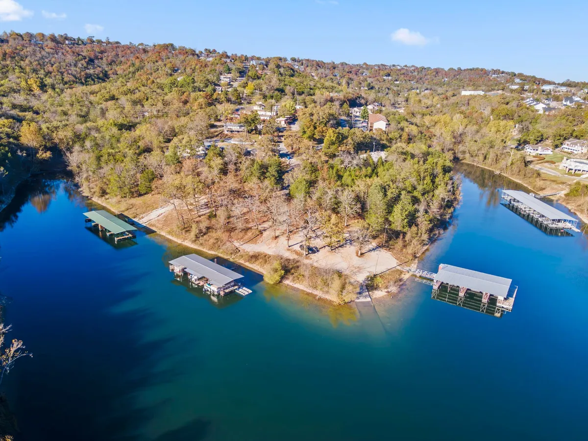A scenic view over Table Rock Lake with boat docks extending into the water, surrounded by lush forest and hillside homes. The image captures boats at the docks and a serene lakeside atmosphere, evoking the essence of a boating and fishing lifestyle.