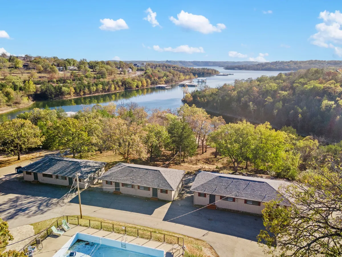 A relaxed exterior lakeside scene showing cabins nestled among trees, a sparkling swimming pool, and the tranquil lake beyond. The setting hints at early morning sunrises and relaxed afternoons by the water, with space for outdoor fun and relaxation.