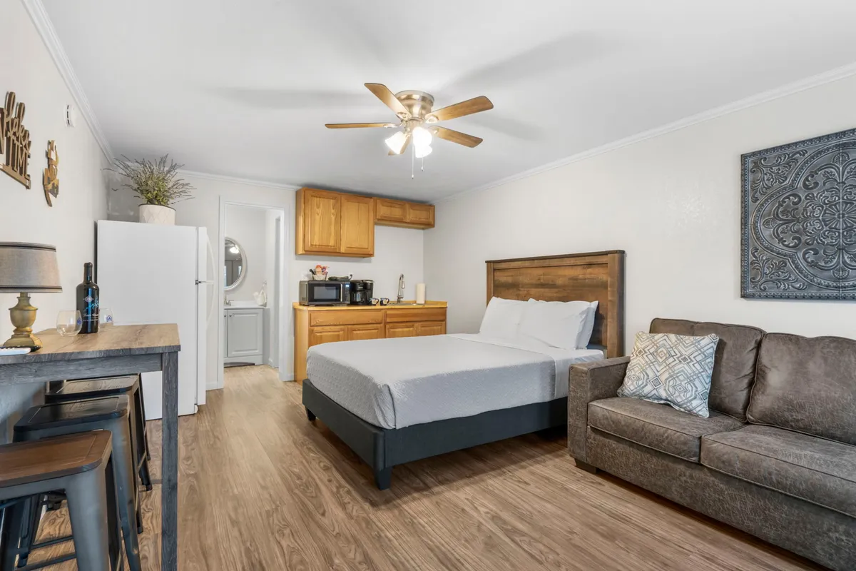 This image depicts a welcoming studio space featuring a plush queen bed, a comfortable sofa, a compact kitchenette, and a small dining table. The layout is open, allowing for easy movement and shared moments. The ambiance is cozy, with soft lighting and neutral tones enhancing the inviting atmosphere.