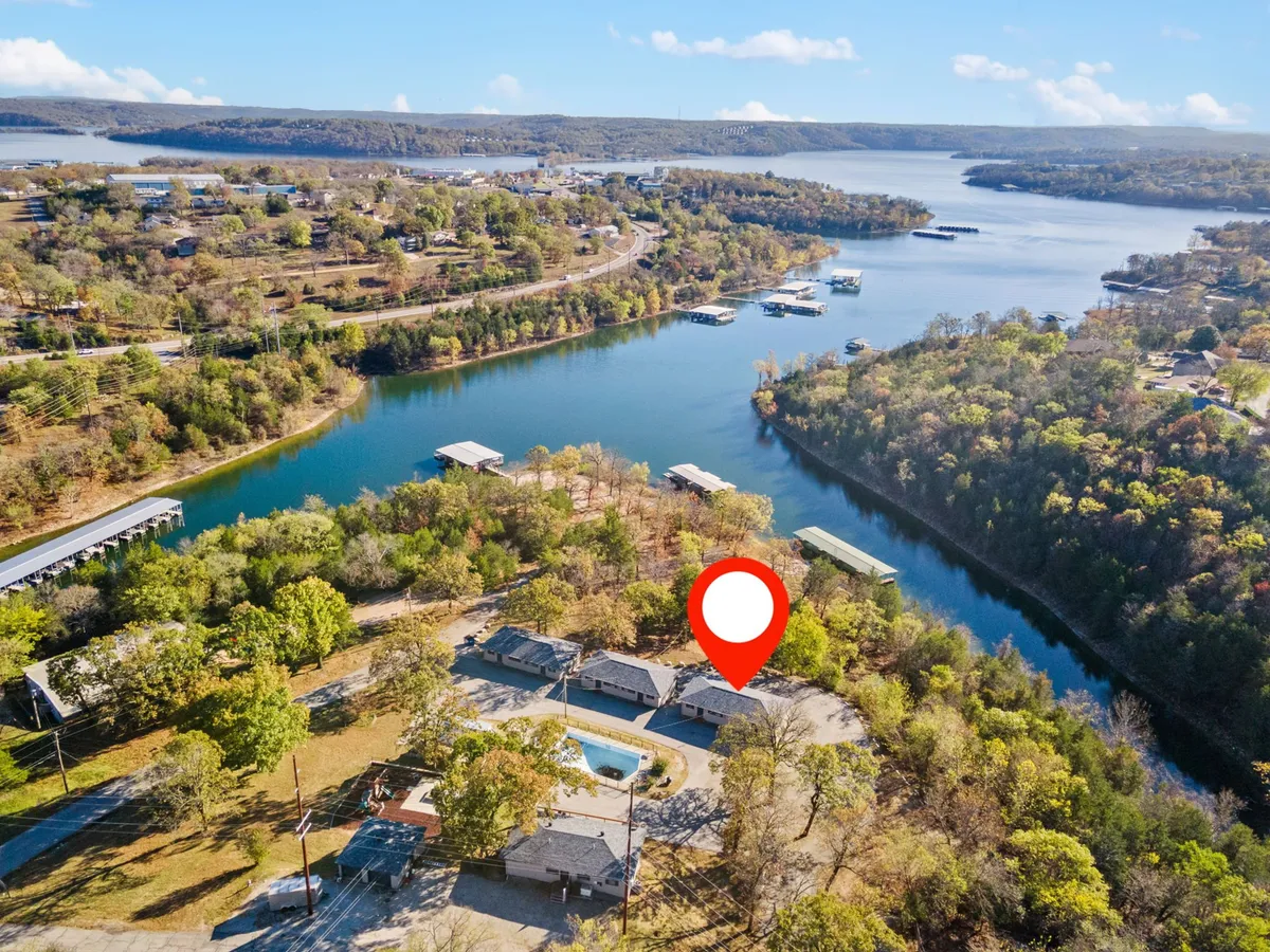 The image showcases an inviting waterfront condo complex set against the tranquil backdrop of Table Rock Lake. The scene captures the shimmering lake at sunset, with lush trees framing the property, a sparkling pool in the foreground, and the potential for lakeside activities such as boating and fishing. Decks with seating areas overlook the water, inviting guests to relax and unwind.