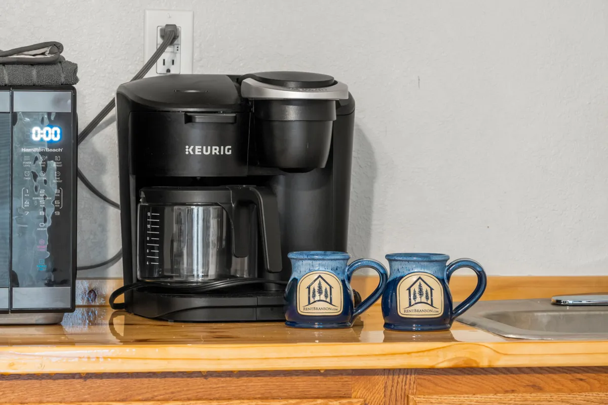 A close-up view of a Keurig coffee maker and two blue mugs on a countertop. The scene is warm and cozy, inviting guests to enjoy a fresh cup of coffee or tea, a staple of any convenient kitchenette.