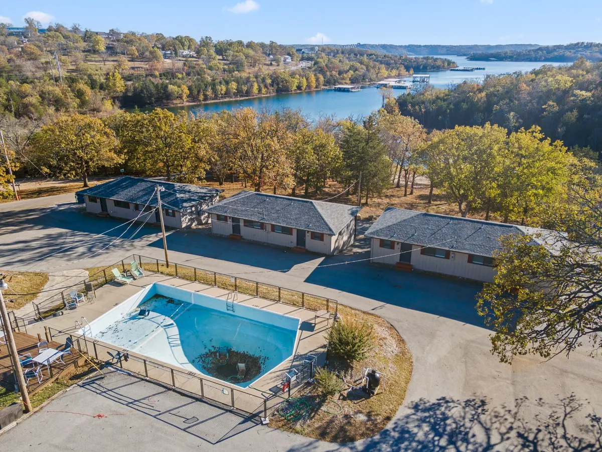 This image captures a picturesque view of a pool overlooking Table Rock Lake, with motel units partially visible and surrounded by trees. The tranquil, lakeside setting invites guests to enjoy both water views and outdoor relaxation.