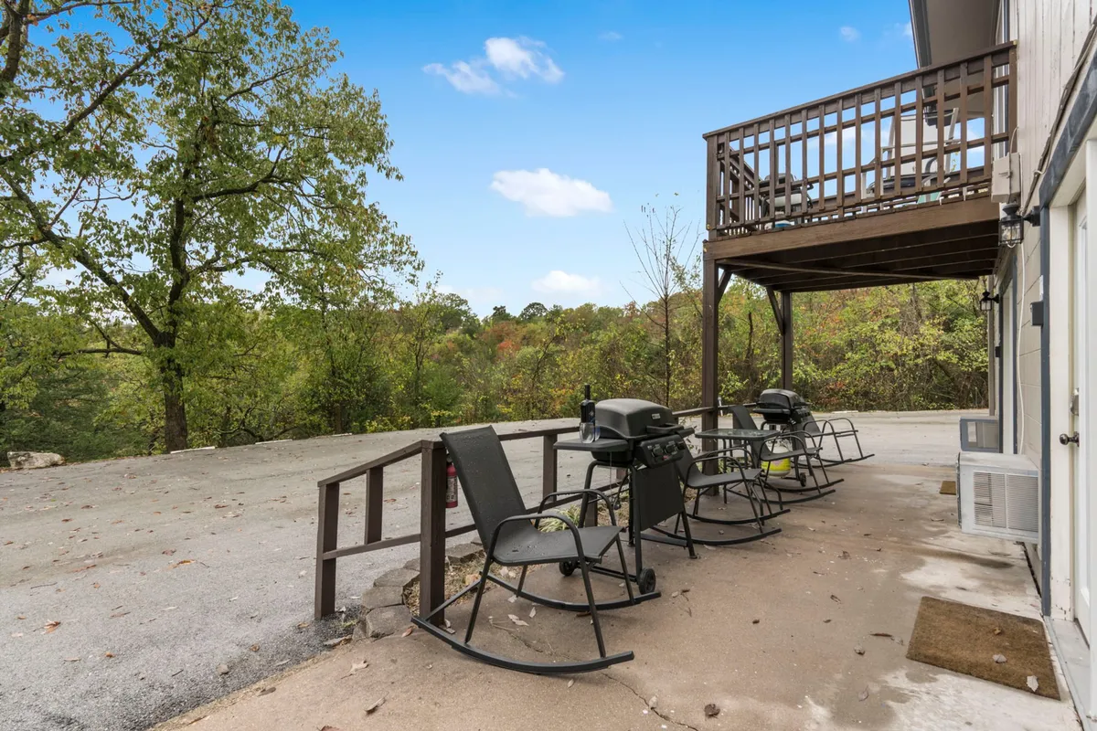 The scene shows inviting rocking chairs on a deck, a grill nearby, and lush trees surrounding the area. The space is designed for relaxation and social connection, with beautiful sunset views and tranquil natural surroundings.