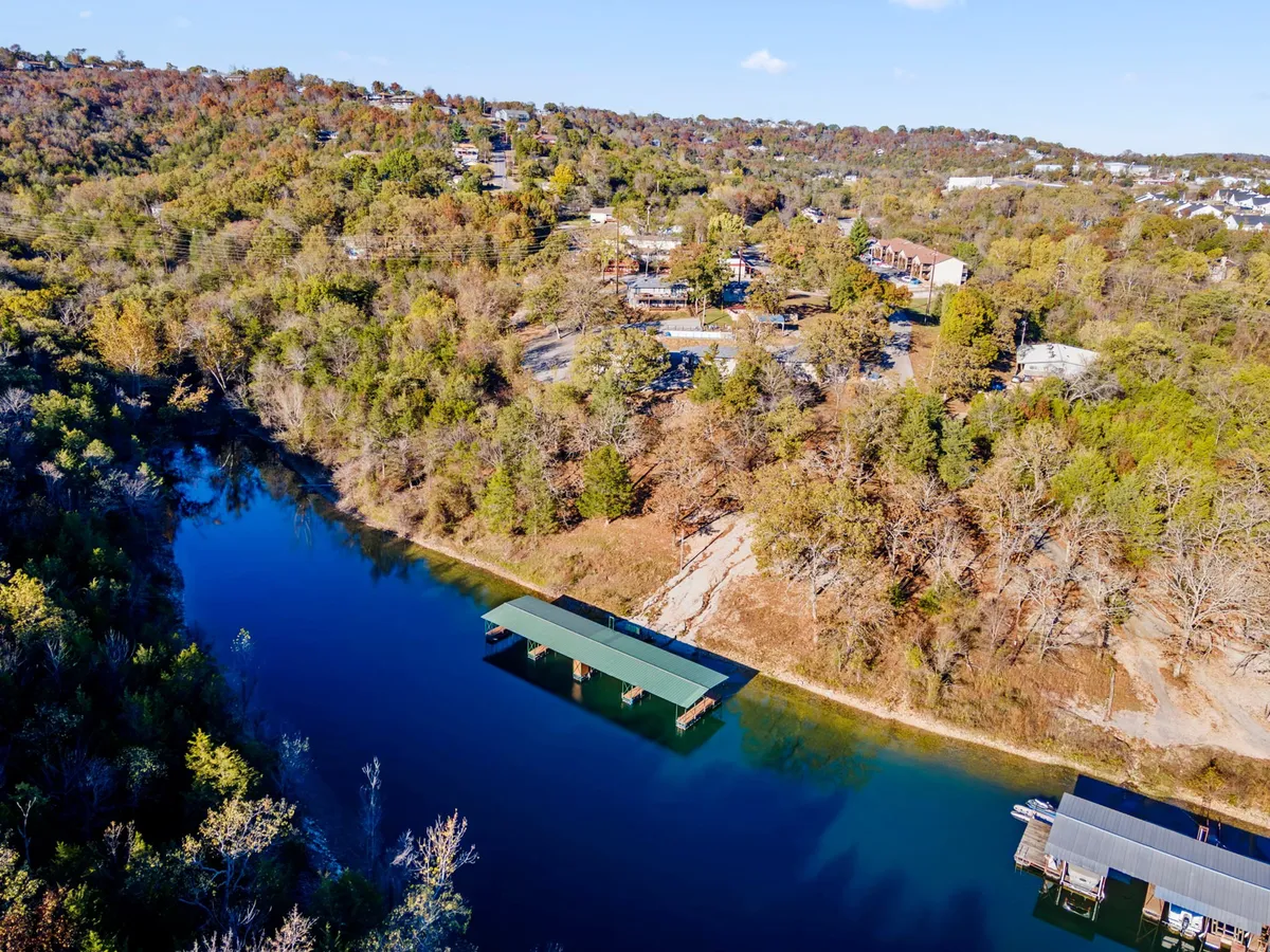 A tranquil lakeside scene featuring a wooden dock stretching over the calm water of Table Rock Lake, with surrounding trees, gentle hills, and houses in the distance. The setting sun casts a golden hue across the landscape, creating a serene and romantic atmosphere.