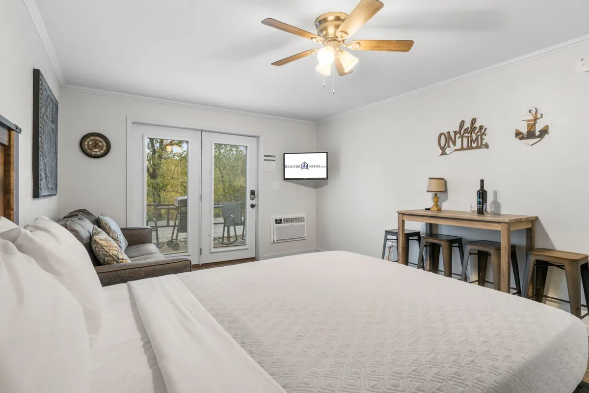 A comfortable, casual studio space featuring a queen bed, a supportive couch, a dining table for shared meals, and sliding doors leading outside. The setup is perfect for families or couples looking to relax, dine, and enjoy evening sunsets from the balcony.