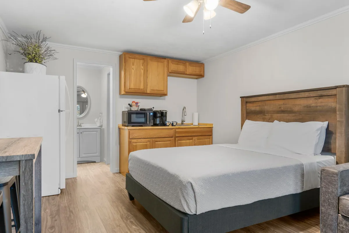This interior shot includes a bed, a tidy kitchenette, a small dining table, and a visible refrigerator. The arrangement suggests ease and comfort, with space for both relaxing and simple food prep. The overall ambiance is warm and welcoming, supporting a sense of home away from home.