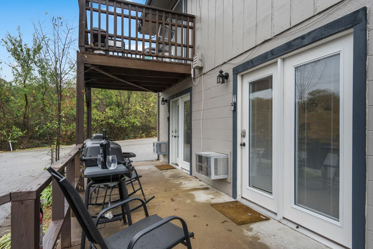 This image features a spacious patio area equipped with multiple grills and a comfortable seating arrangement. The patio sits adjacent to entrance doors, suggesting direct access from the condo. Surrounded by greenery, the setting is perfect for both relaxing and socializing outdoors.